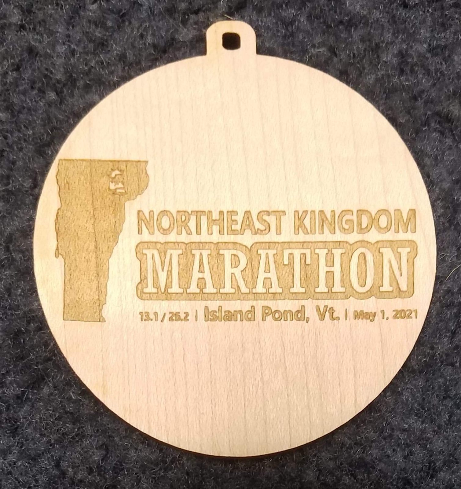 the wooden medal showing the state of Vermont and the words "Northeast Kingdom Marathon 13.1/26.2   Island Pond, VT    May 1, 2021"