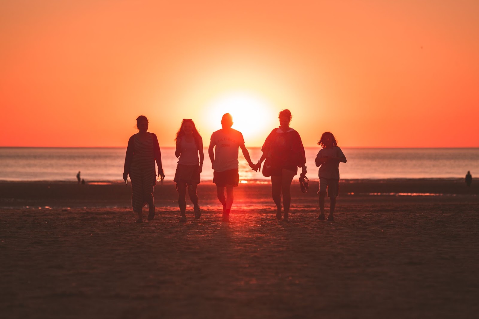 Friends holding hands and walking on beach at sunset