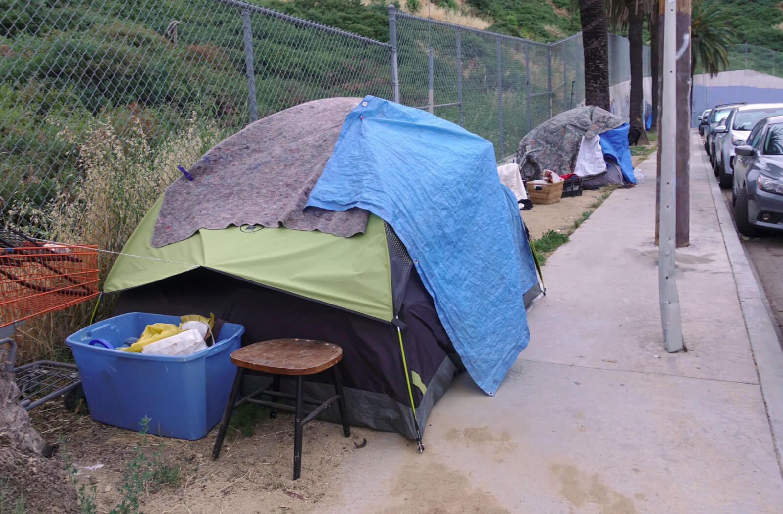 Green and blue colored tents are set up on the side of the road as temporary shelters for homeless individuals.