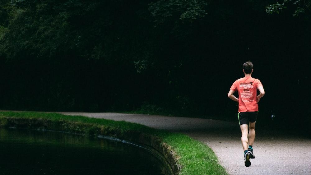 homem de camisa vermelha correndo em pista ao lado de lago