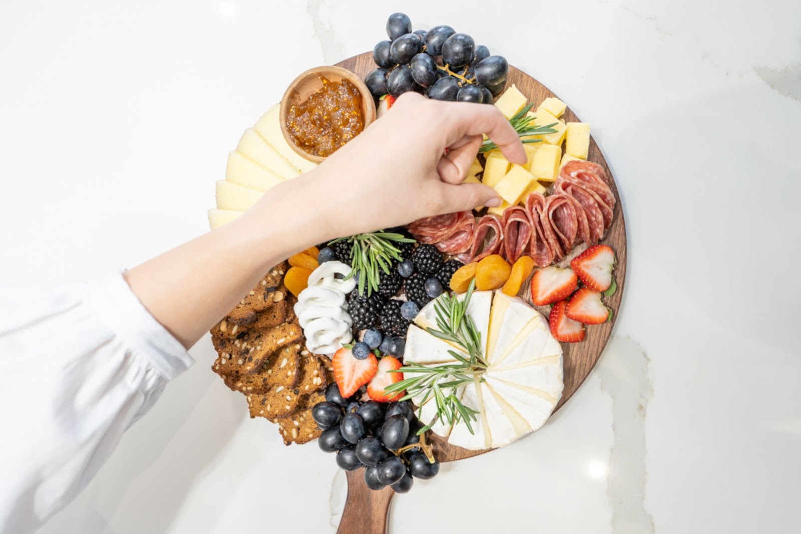 a charcuterie board on a round wood serving board, consisting of cheeses, salami, grapes, blackberries, blueberries, strawberries, crackers, dips and dried fruits