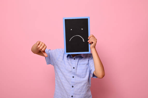 A man covering his face with cardboard that has sad smile icon while doing tumb's down post