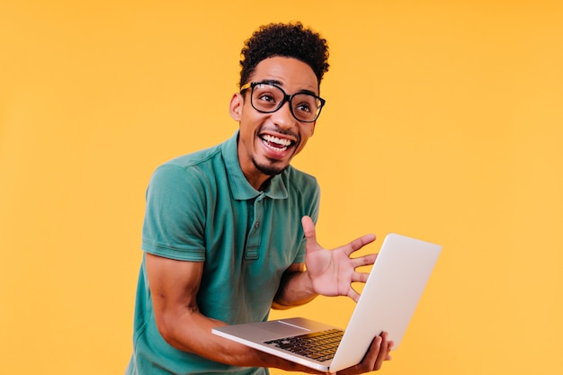 Laughing black man in glasses expressing excitement. emotional international student holding computer.