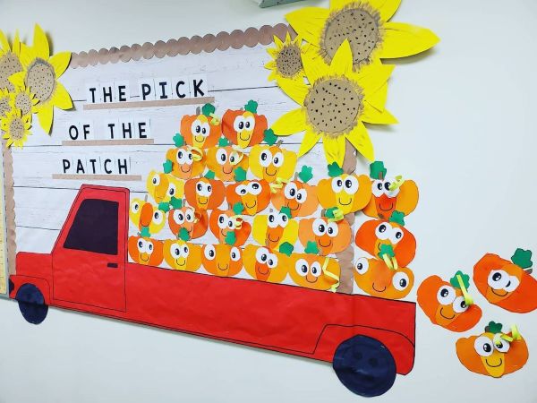 Cute, smiling pumpkin art in a red truck accented with huge sunflowers at top corners of the board