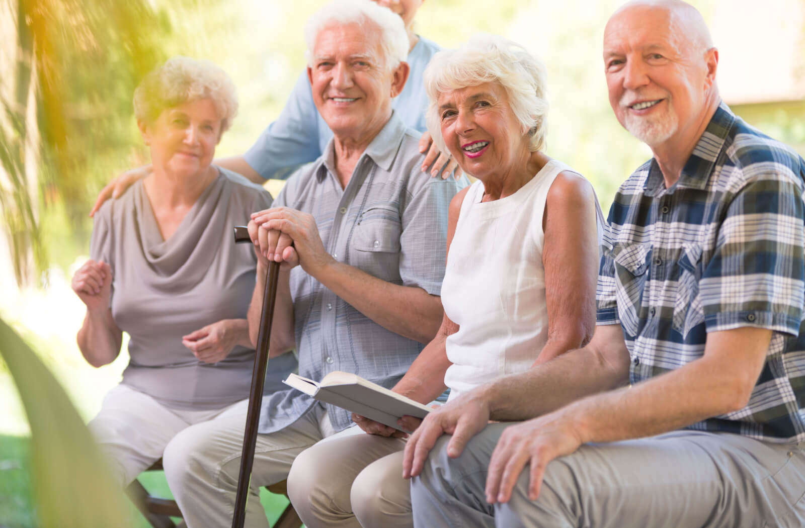 A senior man with a cane with a nurse and other seniors, smiling and looking directly at the camera.