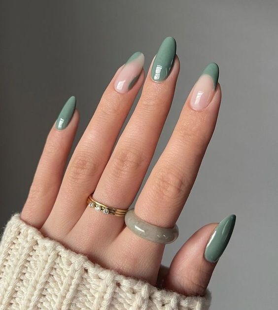 Imagem de uma mão com unhas compridas, arredondadas e decoradas com um esmalte verde claro. A modelo está usando anéis nos dedos.