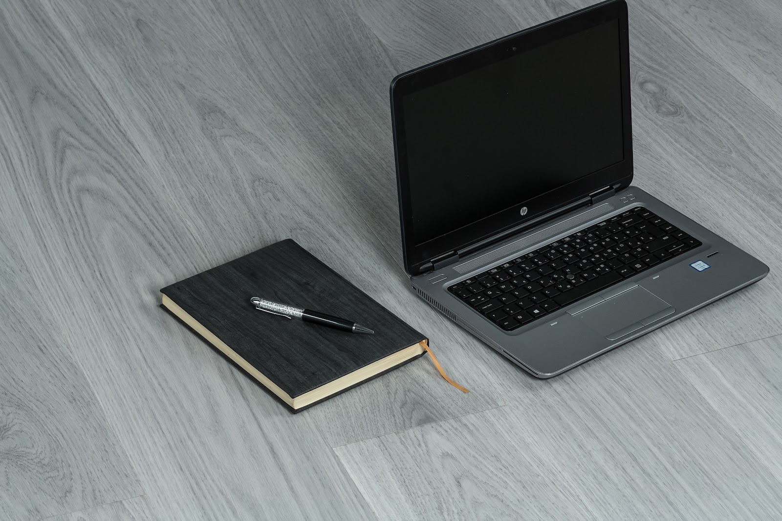 HP Laptop with a book and tilt pen in the wooden desk.