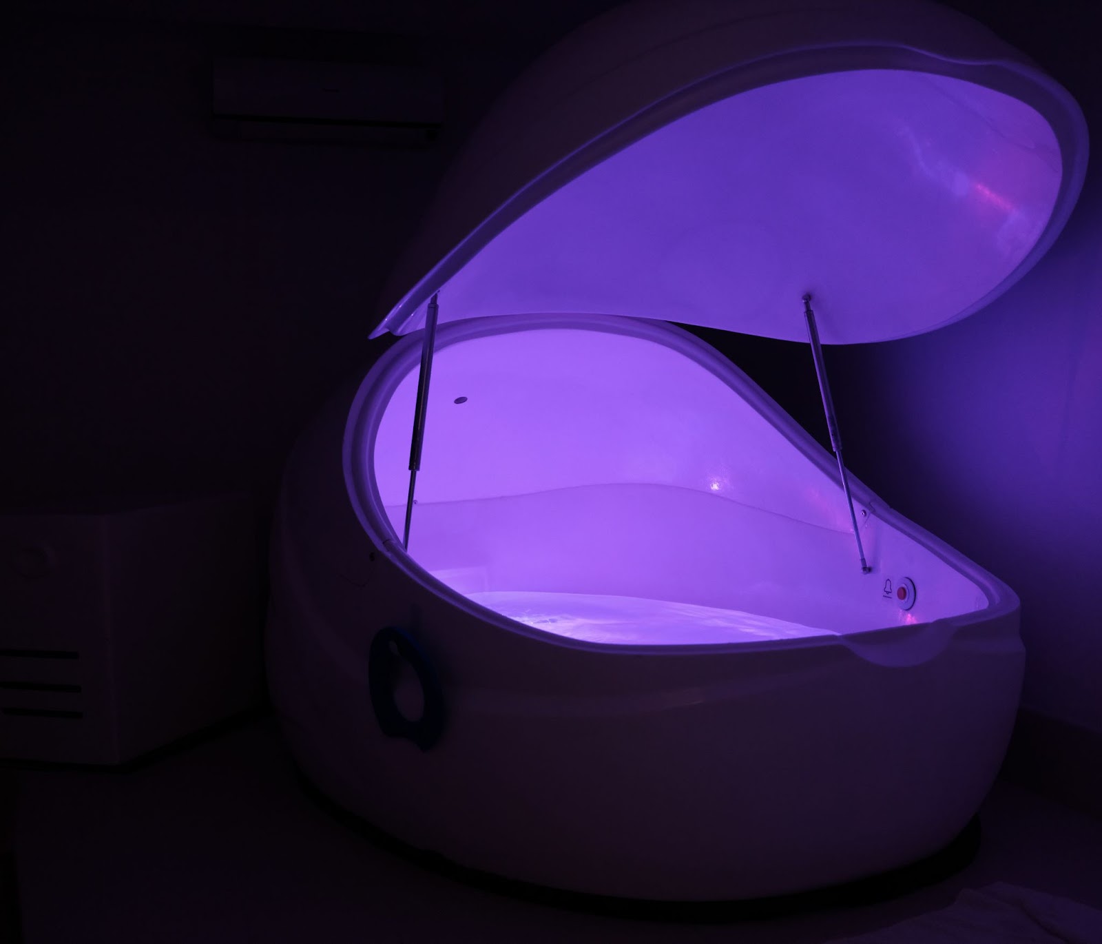 A dark room with a float tank with violet coloured lights.
