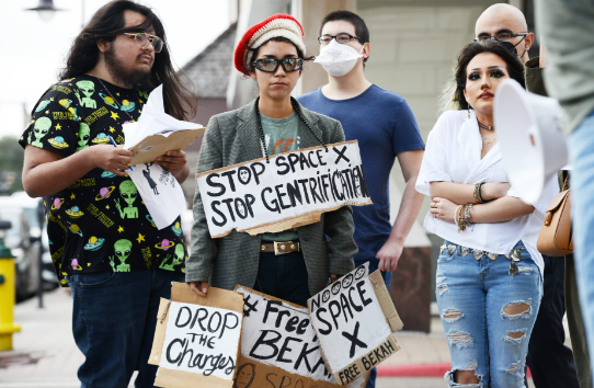 Image of protestors with signs that say "Stop SpaceX, Stop Gentrification", "Drop the Charges" "Noooo SpaceX"