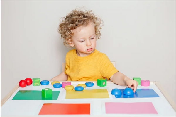 child sitting at table sorting different colored blocks by color