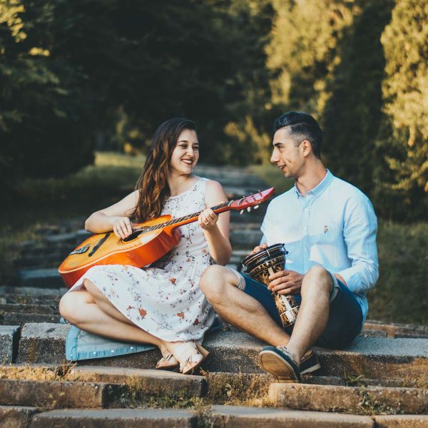 Mujer tocando la guitarra y hombre tocando un instrumento percusivo en el parque