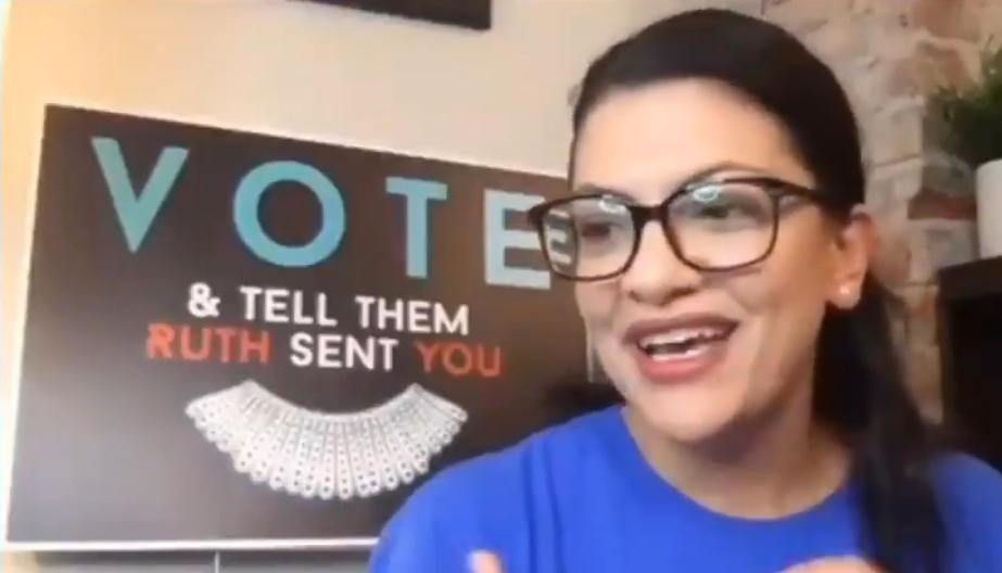 Image of Rashida in front of a sign that says 'VOTE & tell them RUTH sent YOU'