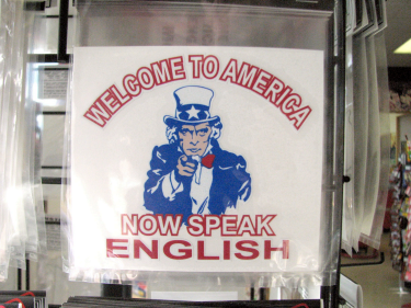 Sign that says "Welcome to America, Now Speak English" with an image of Uncle Sam in the middle. Appears to be for sale at a gift store. 