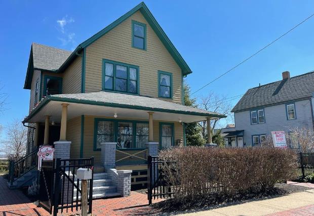 a yellow house with green trim and a black fence