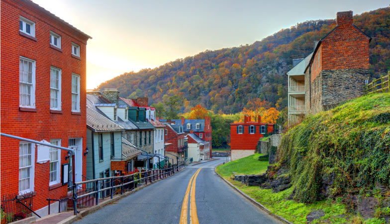 Harpers Ferry, West Virginia, at sunset. Bright red brick buildings along a mountain road. The trees on the mountain are changing colors with the season.