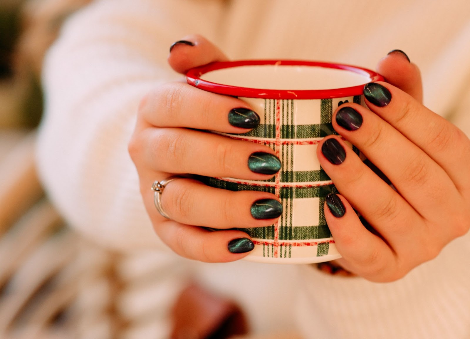Person holds red and red plaid mug and shows off their green tiger eye nails 