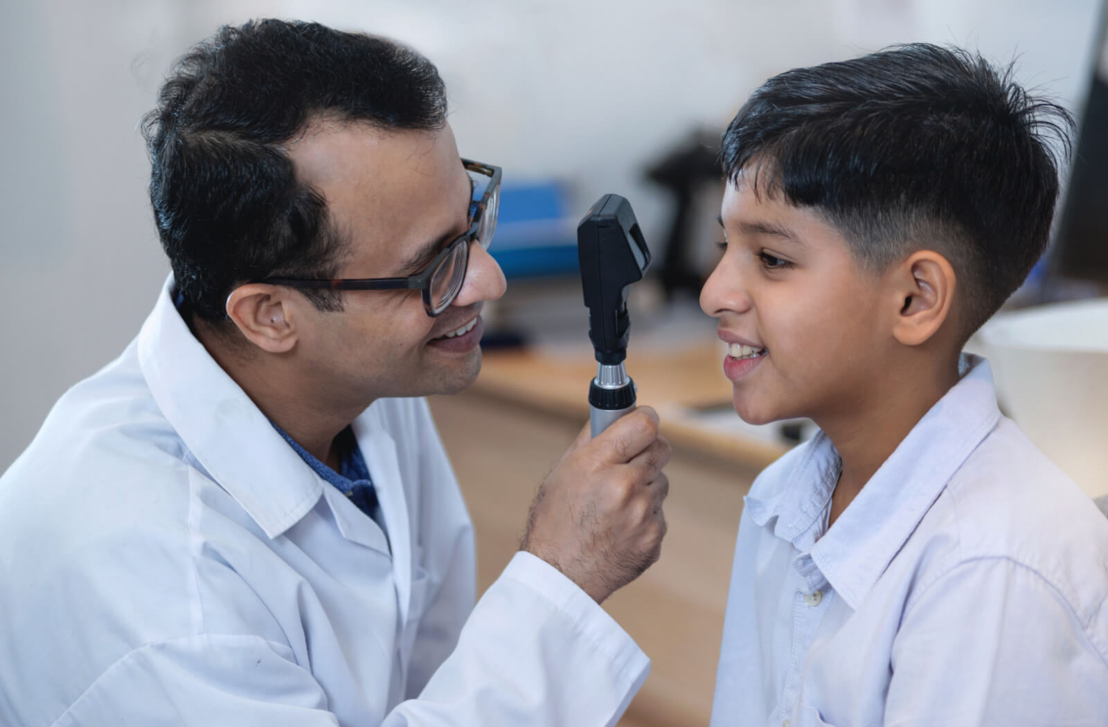 An optometrist smiling and conducting an eye exam on a child using a device that tests his vision