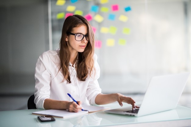 Successful businesswoman working hard on laptop computer in her office dressed up in white clothes Free Photo