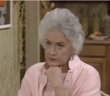 Dorothy from The Golden Girls sitting at the table in the kitchen turning to look at someone behind her with an unamused expression.