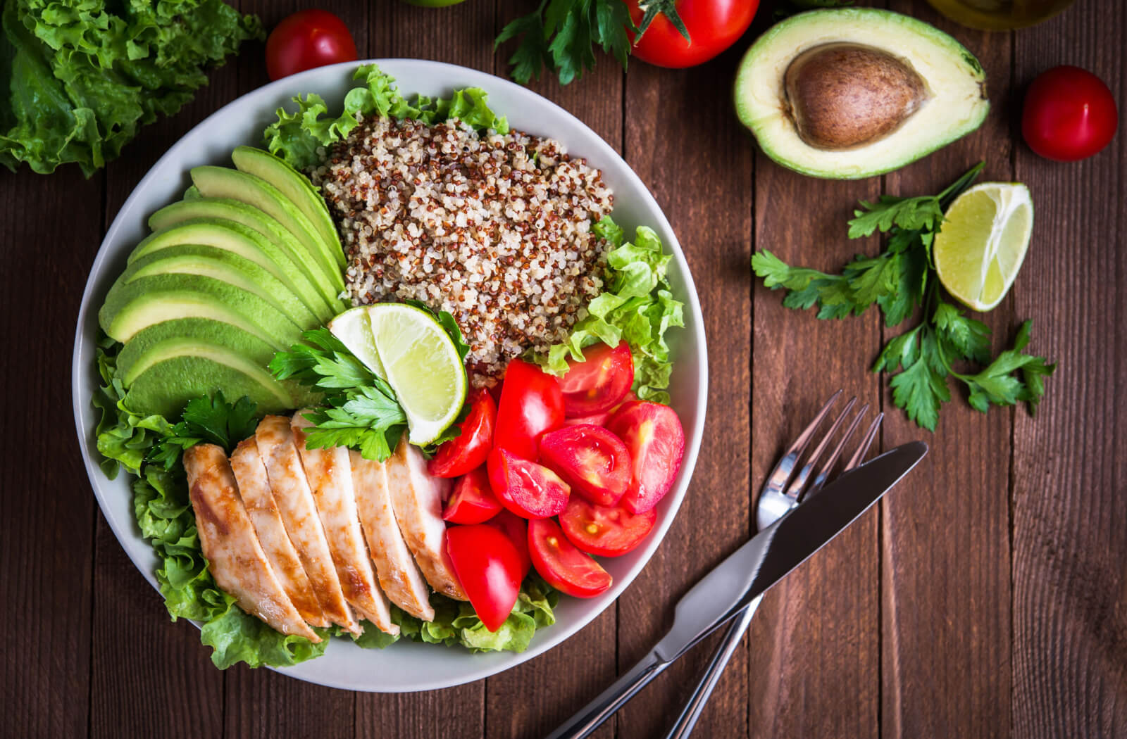 A close-up of a plate of a healthy meal, a roasted chicken, slices of avocado, tomatoes, lime, lettuce, and quinoa. A good balance diet can promote ideal weight and reduce inflammation.