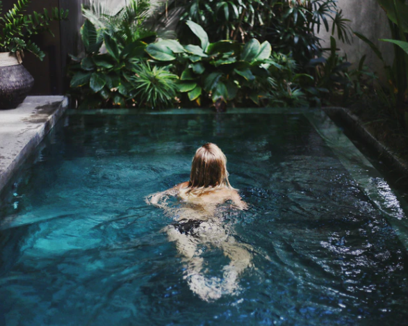 girl in plunge pool in front of green leaves