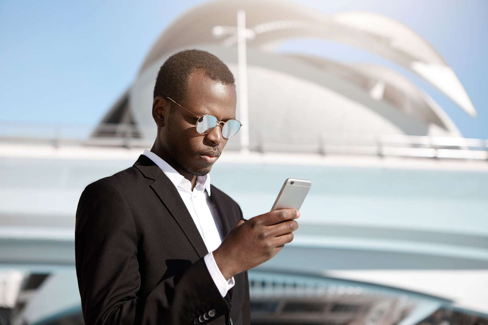 foto de um homem com roupas sociais e óculos escuros, mexendo em seu smartphone para realizar atividades de teletrabalho na modalidade remote everything