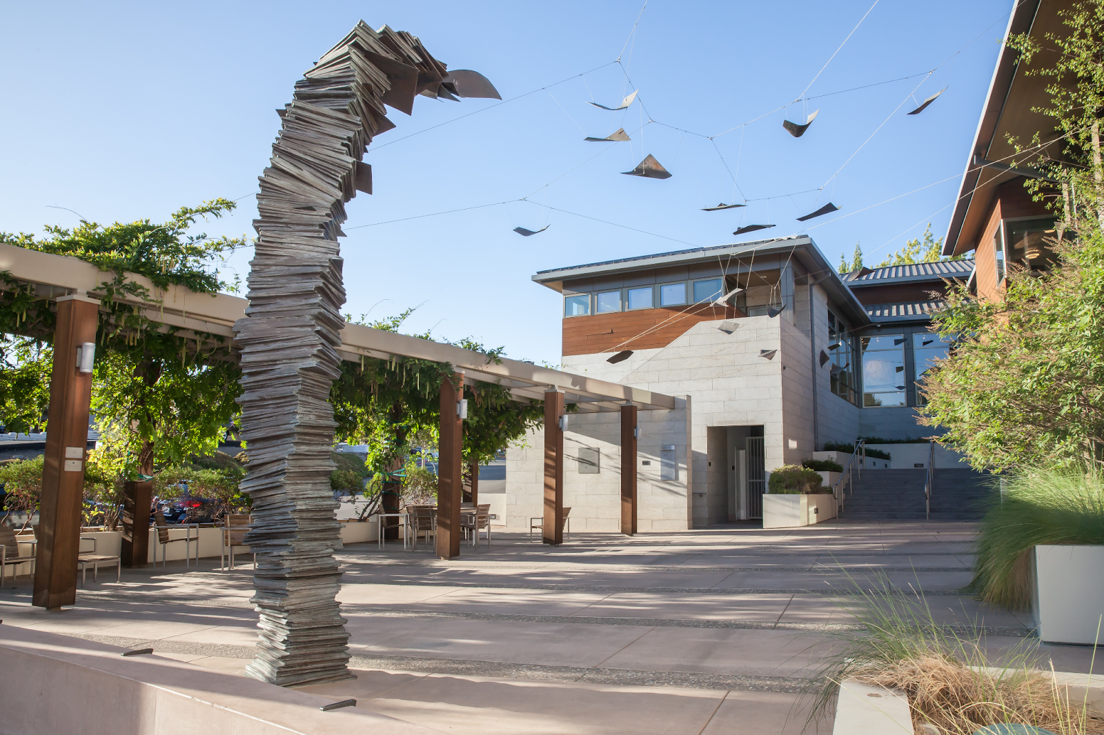 large bronze sculpture of pages outside of the Lafayette Library in California. Single bronze sheets of paper are suspended over an outdoor walkway on wires 