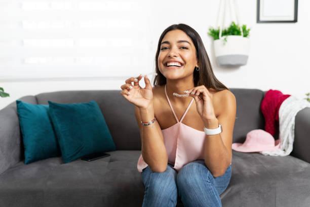 Cute woman happy about dental treatment Portrait of a beautiful Hispanic woman looking happy and smiling while holding a couple of dental retainers for her orthodontics treatment invisalign oral health stock pictures, royalty-free photos & images