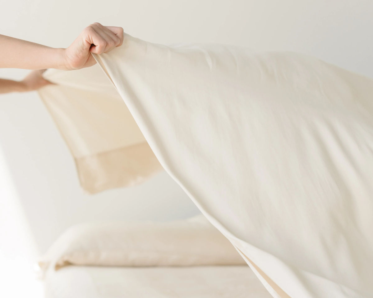 Off-white sheet being draped over bed