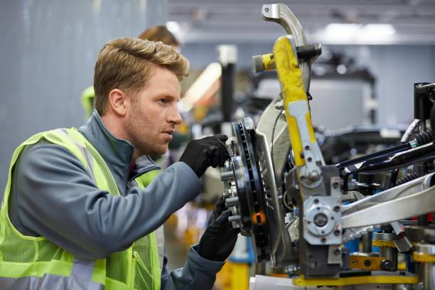 Confident male engineer examining car chassis Confident mid adult engineer examining car chassis at automobile industry. Handsome male supervisor is working on car part in factory. He is wearing reflective clothing. Automobile Engineering stock pictures, royalty-free photos & images