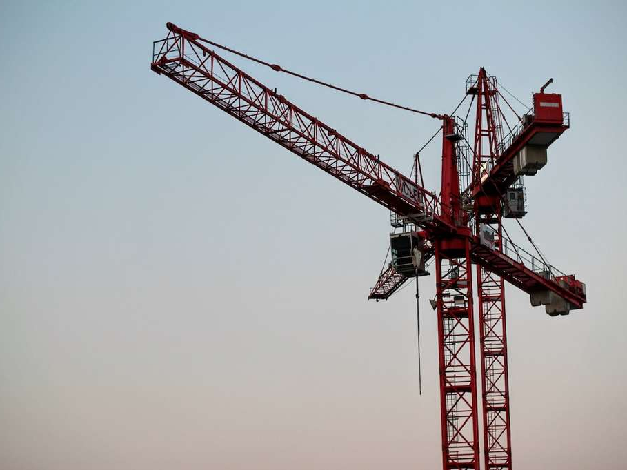 A large red and black tower crane ready to lift construction materials.