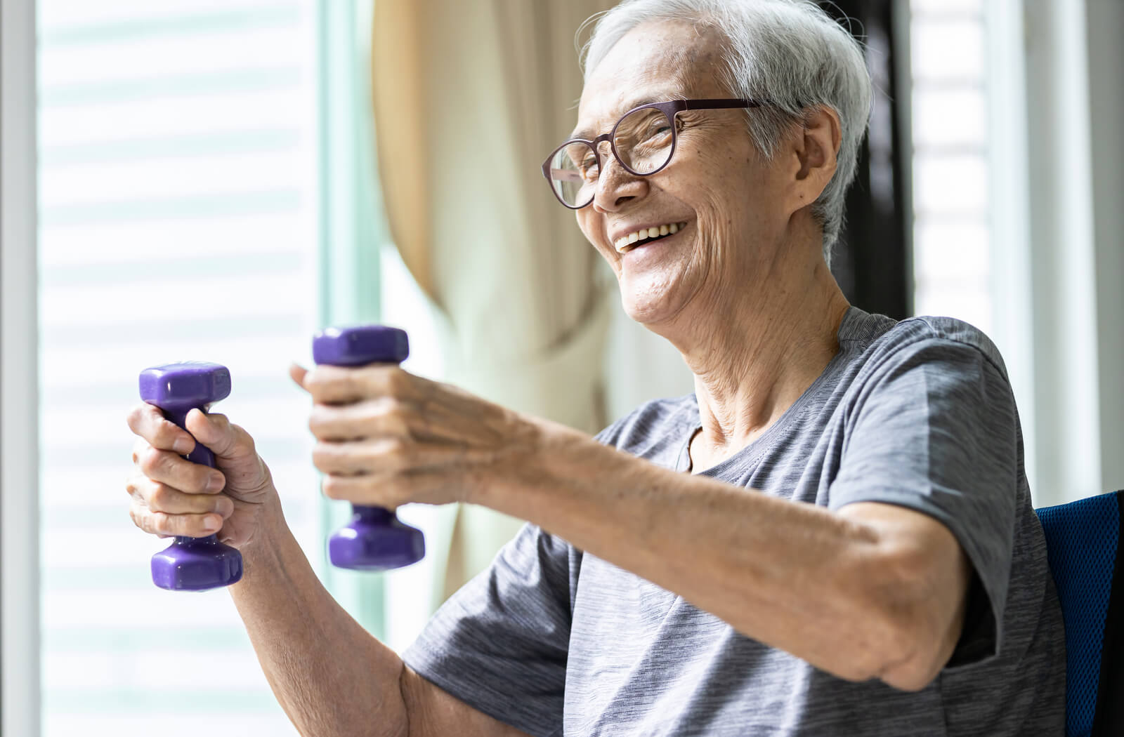 a senior smiles while lifting two hand weights