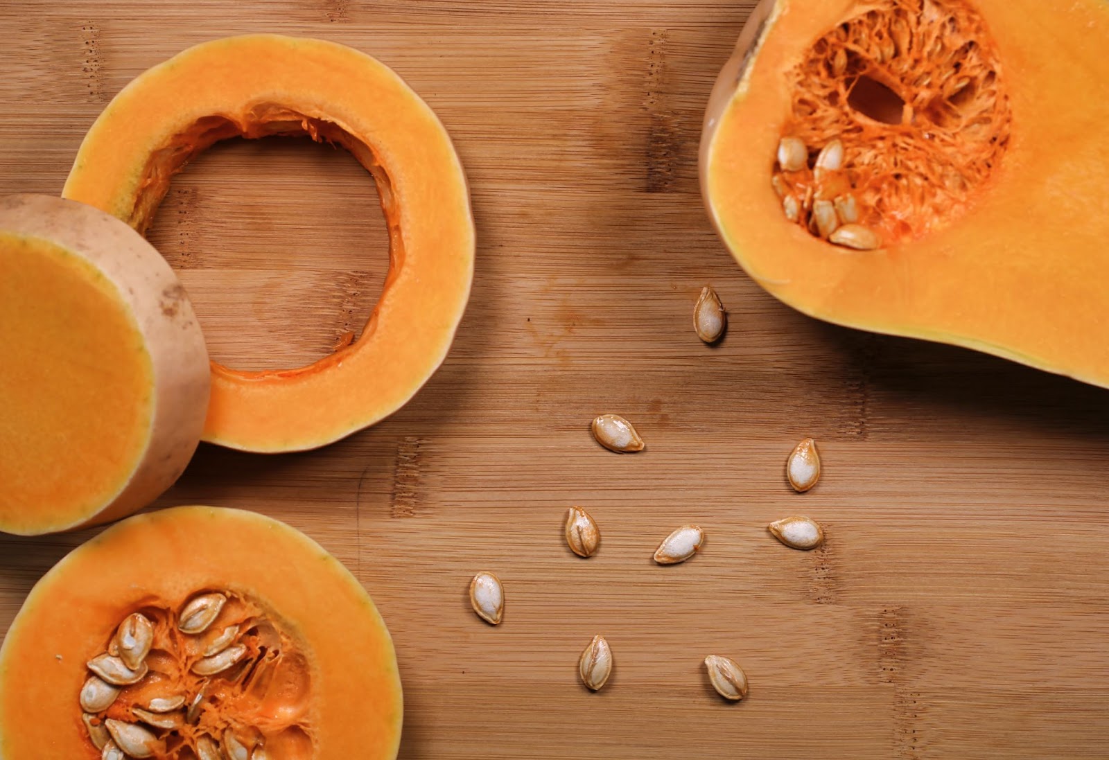 A sliced pumpkin, with some seeds scattered about the table.