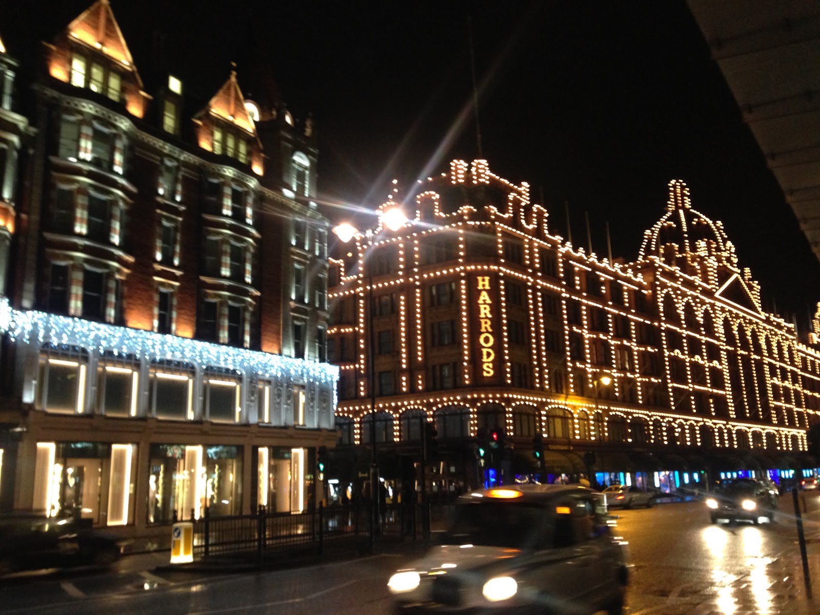 harrods luxury department store in london. Decorative lighting on the building's exterior facade seen during night time, london taxi passing the street in foreground.