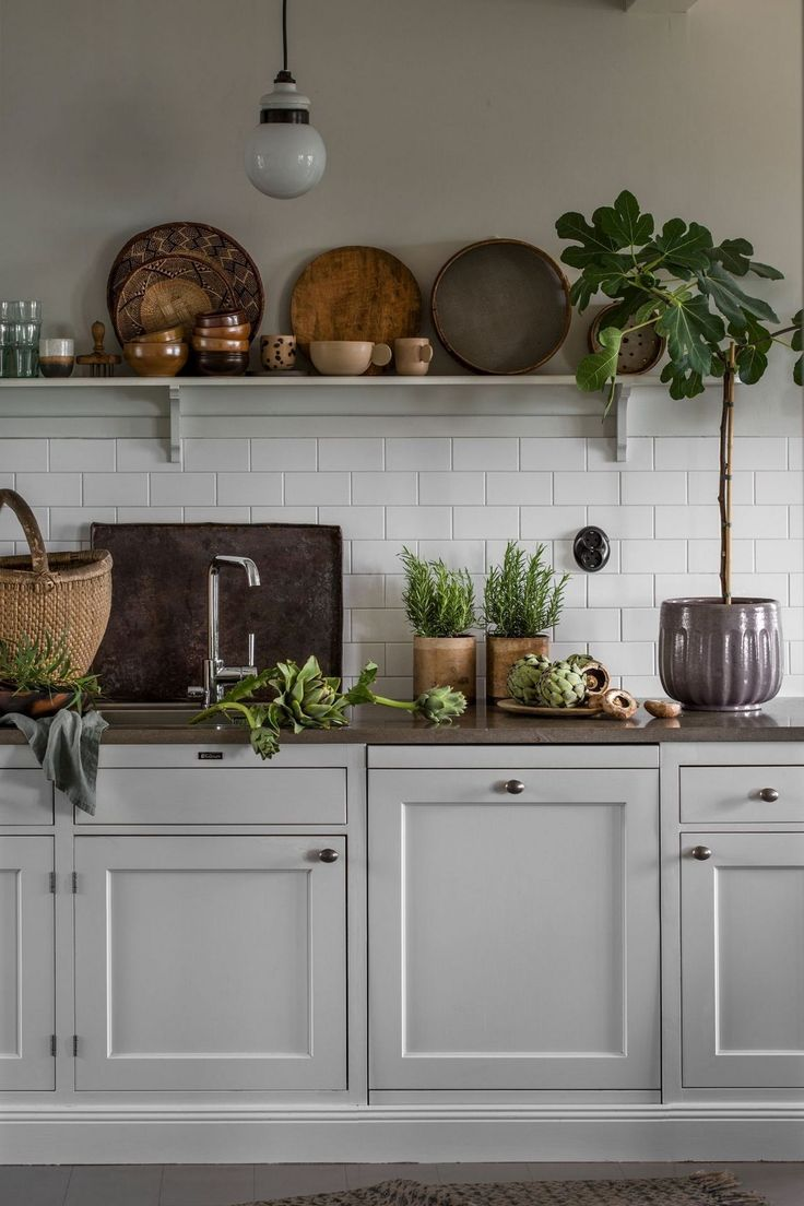 rustic scandinavian kitchen with open shelving, white shaker cabinets, white subway tile backsplash, minimalist hardware, potted plants and decorative dishware