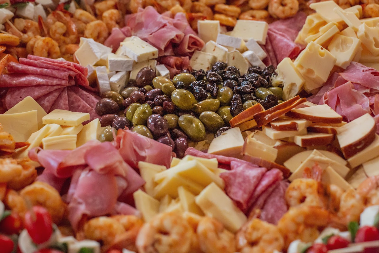 a closeup of a charcuterie spread with meats, cheeses, olives, shrimp and dried fruits