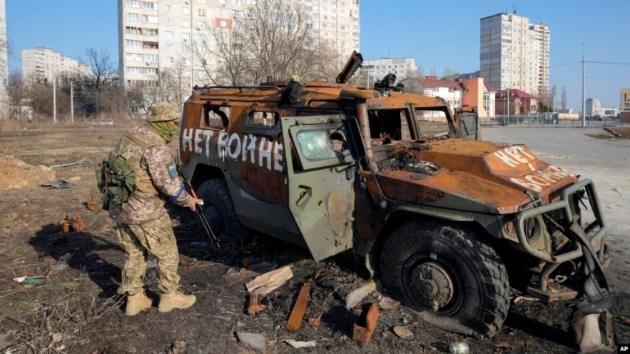 Binh sĩ Ukraine bên cạnh 1 xe chở quân của Nga bị tiêu diệt ở gần Kharkiv hôm 24/3.