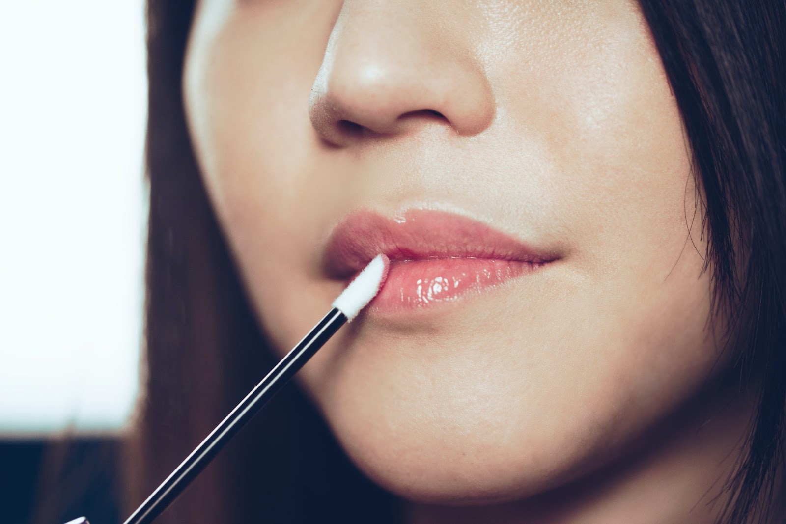 Close up of a woman applying clear lip gloss