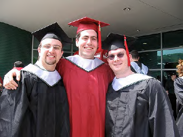 3 young men with graduation gowns and mortarboards, smiling and posing for the camera.
