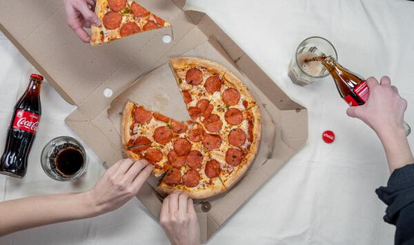 Foto tirada de cima de uma pizza e mãos pegando alguns pedaços