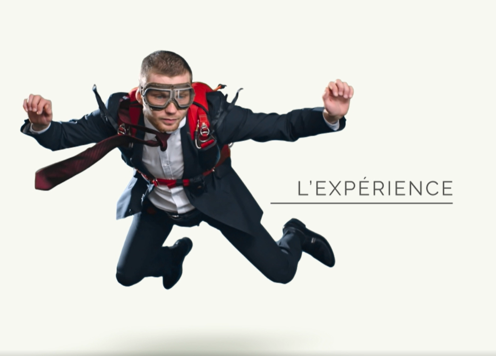 homme sautant en parachute, habillé d’un costume trois pièce, accompagné de la mention “L’expérience”.