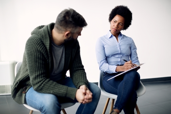 black-female-psychotherapist-taking-notes-while-talking-man-during-counselling