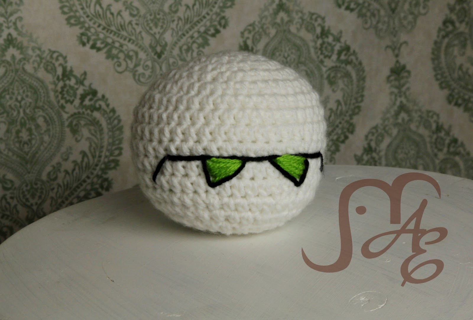 White crocheted ball with green triangles as eyes. 