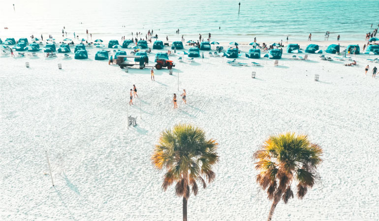 Locals and tourists enjoy a sunny day at Clearwater Beach in Tampa Bay, Florida. The sand is white and fluffy and the water is calm.