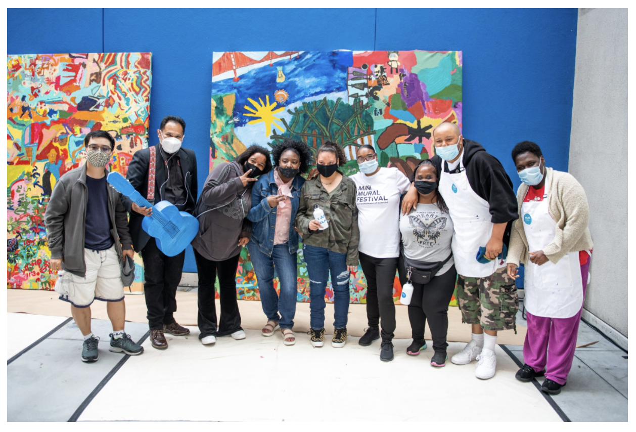 A group of NIAD studio artists posing in front of a brightly colored mural.