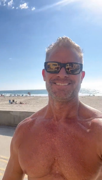 Greg Dixxon taking a selfie outside shirtless on the California boardwalk near venice beach, USA