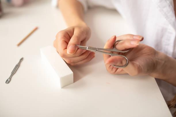 Young woman cutting cuticle with nail scissors at home Young woman cutting cuticle with nail scissors at home nail cuticles stock pictures, royalty-free photos & images