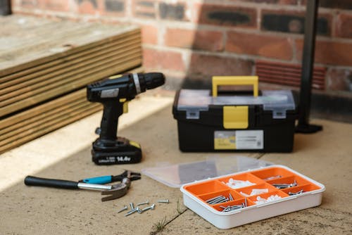 Free Electric screwdRiver 2 on floor near containers with instruments placed near spanner with hammer against brick wall  and wooden barrier Stock Photo