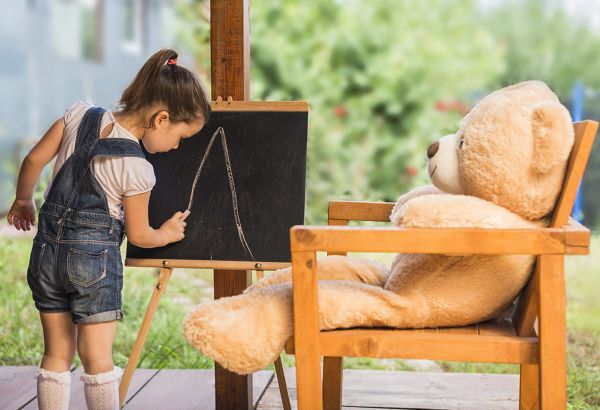Little girl pretending to teach her bear and draw a letter A on her easel