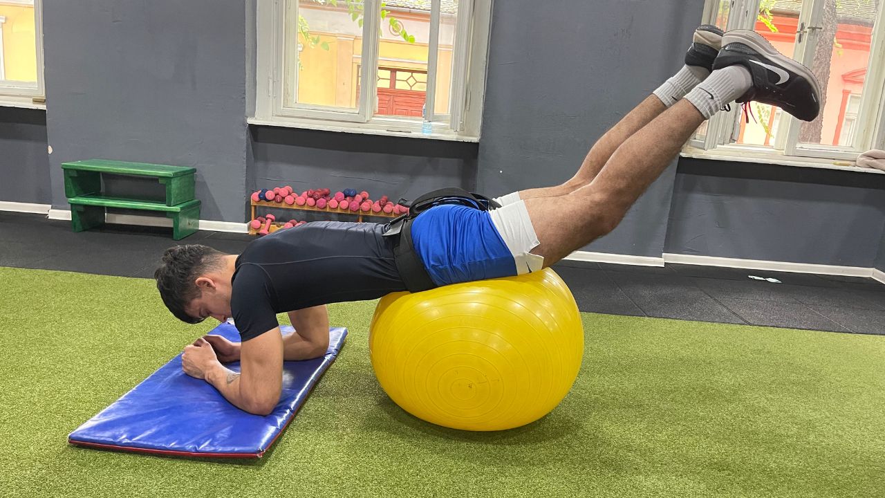 Vanja performs a stability ball reverse hyperextension exercise for the lower back in the commercial gym setup.